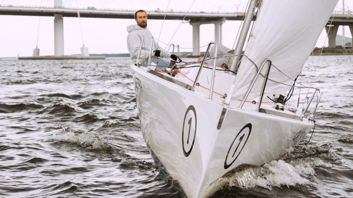 Zo maak je jouw jacht klaar voor een overtuigende eerste indruk Ervaar de spanning van zeilen met een zeeman die een schip navigeert onder een opvallende brug.